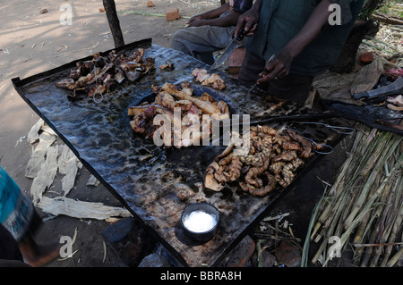 Ein lokaler Straßenhändler bereitet gegrilltes Fleisch und Tierinnereien an einem Imbiss im Freien in einer ländlichen Siedlung in Malawi, Afrika zu Stockfoto