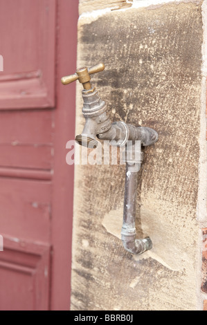 Messing-außen/außen Dienstprogramm Wasserhahn ausgestattet, um strukturierte Sandsteinmauer neben verblasste Holztür Stockfoto