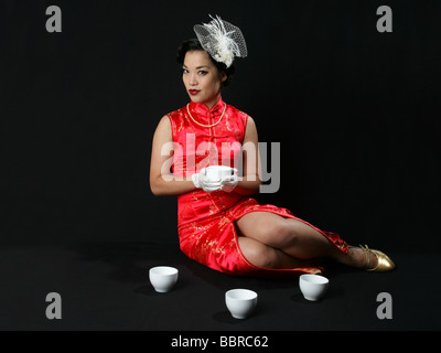 Pin-up Portrait Burlesque Darsteller Marianne Käsekuchen in einem langen chinesischen Kleid mit weißen Hut und Handschuhe halten eine Teetasse