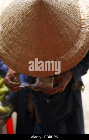 Alten Vietnamesin tragen [kegelförmiger Hut] Geldzählen, nach vorne gebeugt ' an ' Hoi an, Vietnam Stockfoto