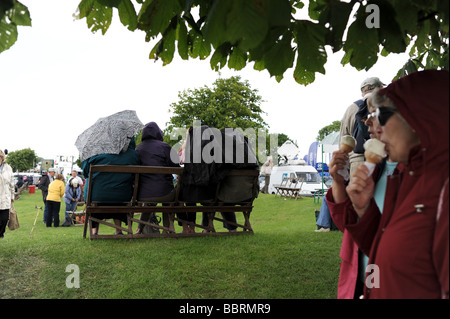 Typisch britische Sommertag als Menschen bekommen unter Sonnenschirmen und Schutz vor Regen auf den Süden von England Show Stockfoto