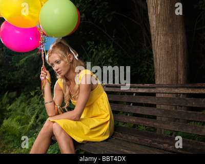 Trauriges Mädchen sitzen auf einer Bank mit einem Bündel von bunten Luftballons Stockfoto