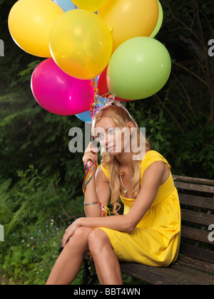 Trauriges Mädchen sitzen auf einer Bank mit einem Bündel von bunten Luftballons Stockfoto