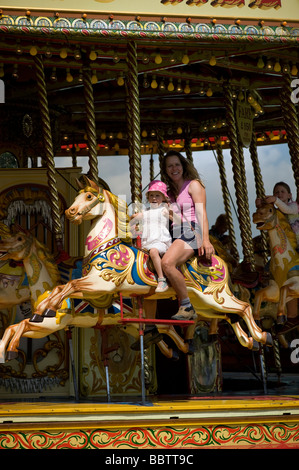 Mutter und junge Tochter reiten auf Dampf Galloper Festplatz Kreisverkehr Stockfoto