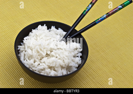 Weißer Reis in einer schwarzen Schale mit zwei Stäbchen Stockfoto