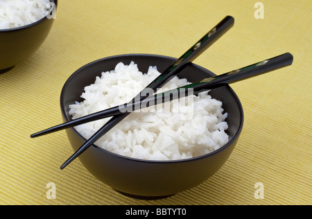 Weißer Reis in einer schwarzen Schale mit zwei Stäbchen Stockfoto