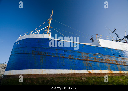 Gestrandeten Schiff, blau auf blau. Ein altes Holzschiff gestrandet im Hafen blau gegen eine Trockenfäule blauen Himmel. Stockfoto