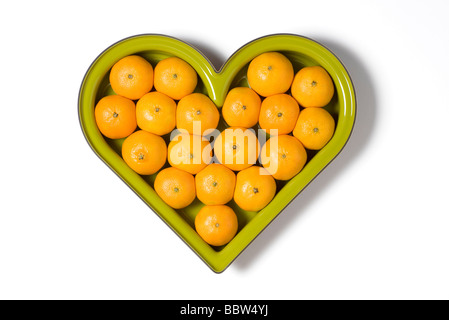 herzförmige grüne Obstschale voll von Orangen Stockfoto