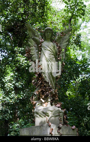 Viktorianische Architektur Engel vor einem Grabstein, nun bedeckt im Unterholz in Nunhead Friedhof überwuchert Stockfoto