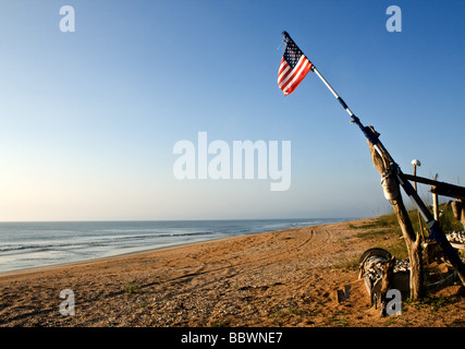 Alten zerrissenen amerikanische Flagge auf einem provisorischen Mast auf einem einsamen Strand mit strahlend blauem Himmel Stockfoto