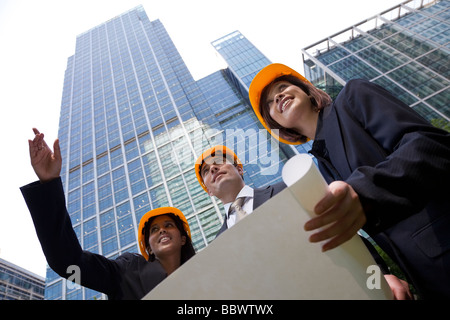 Eine Gruppe von drei Führungskräften ein Mann und zwei Frauen tragen Schutzhelme überprüfen Baupläne in einer modernen Stadt Stockfoto