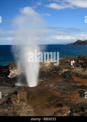 Der Ausbruch des Nakalele Blasloch auf der Nordküste von Maui, mit Wasser hoch in die Luft geblasen, Leute zuschauen. Stockfoto