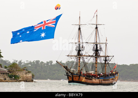 Replik von Captain Cooks Segeln Schiff HM Bark Endeavour im Hafen von Sydney, mit einer großen australischen Flagge in der Nähe. Stockfoto