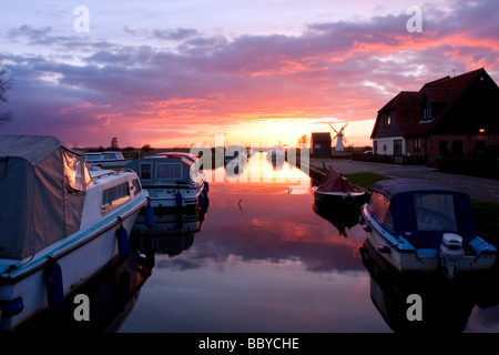 Staithe und Boote Thurne Deich mit Thurne Windmühle im Hintergrund bei Sonnenuntergang auf den Norfolk Broads Stockfoto