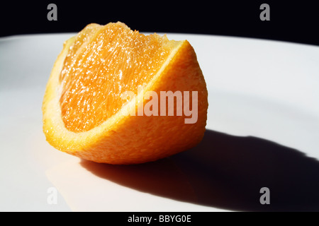 Orangenscheibe auf einem weißen Teller im Sonnenschein Stockfoto