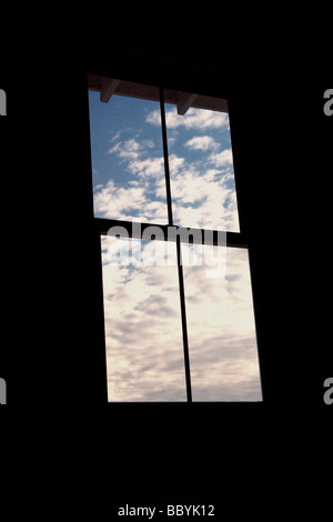 Dunklen Raum mit einem Fenster mit blauem Himmel und Wolken außerhalb Stockfoto