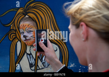 Fünf Jahres altes Mädchen mit Gesicht gemalt haben ihr Foto von ihrer Mutter mit einem Mobiltelefon im Vereinigten Königreich Stockfoto