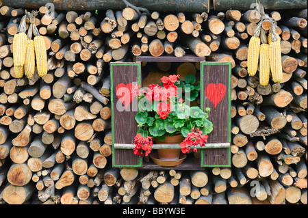 Replik eines Fensters mit Herzen, Fensterläden, Geranien und Maiskolben in einem Stapel Brennholz, Slowenien, Europa Stockfoto