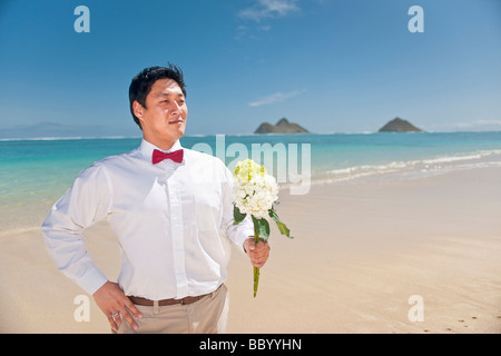 Asiatischer Bräutigam wartet auf seine Braut mit einem Blumenstrauß bei einem Spaziergang am Strand von Lanikai Kailua Hawaii Stockfoto