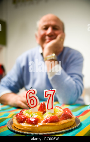 Porträt des älteren Menschen mit Kuchen auf 67. Geburtstag Stockfoto