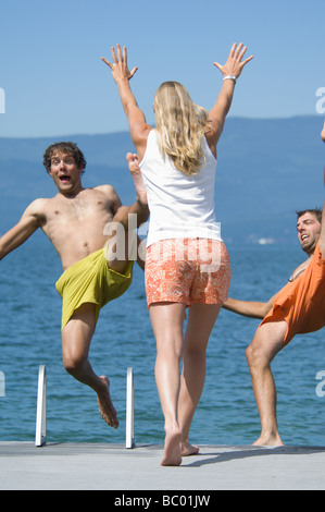Eine junge Frau drückt ihre männlichen Freunde in einen See. Stockfoto