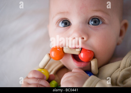 drei Monate altes Babymädchen greifen und Maul ein Beißring gemacht von Holzperlen, kauen auf Spielzeug Stockfoto