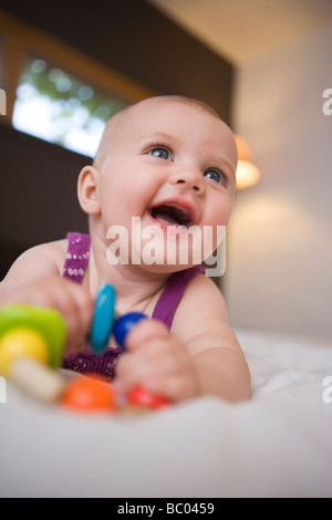 drei Monate alten Säugling Mädchen lächelnd halten Sie hölzerne Kinderkrankheiten Perlen, auf einem Bett Stockfoto