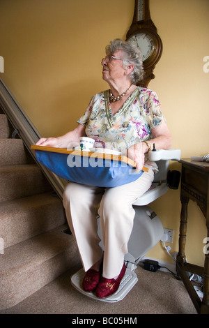 Eine alte Dame nutzt eine Sessellift und die Treppe hinunter in ihr Zuhause mit ihrem Frühstück zu bewegen Stockfoto