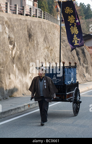 Ein Mann mit Festival Kleidung zieht einen traditionellen Karren mit Banner während des Frühlingsfestes in Takayama Japan Stockfoto