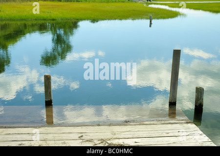 Eine alte hölzerne dock in einem Salz-Sumpf in Connecticut mit Cumulus-Wolken spiegeln sich in das blaue Wasser mit glatten cordgrass Stockfoto