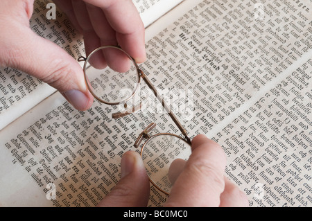 Hände halten ein paar Kneifer Brille über schwedische Bibel. Stockfoto