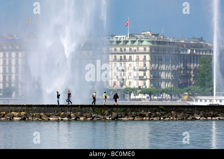 Fußgänger schlendern unter dem strömenden Wasser auf den Jet d Eau Brunnen auf einem Steg in den Genfer See Genf Schweiz Stockfoto