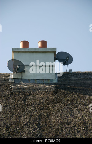 Zwei Fernseher Satellitenschüsseln auf dem Schornstein eine strohgedeckte Hütte, Devon, UK Stockfoto