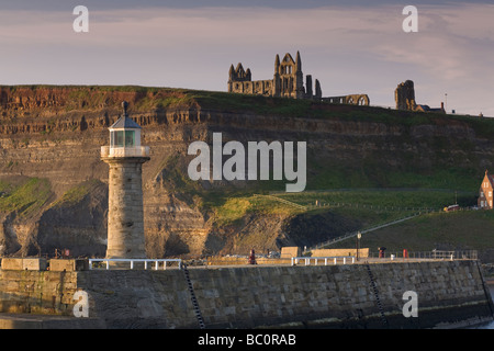 Der Leuchtturm auf Whitby Pier mit St. Hilda Abtei auf den Klippen im Hintergrund Stockfoto