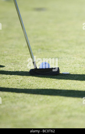 Eine Nahaufnahme von einem Putter richten Sie hinter einem Golfball auf einem Golf grün, mit dem Loch sichtbar in der Ferne. Stockfoto