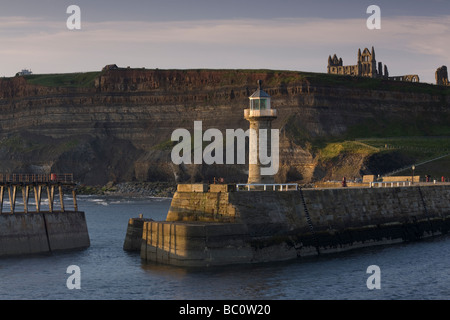 Der Leuchtturm auf Whitby Pier mit St. Hilda Abtei auf den Klippen im Hintergrund Stockfoto