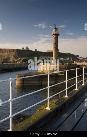 Der Leuchtturm auf Whitby Pier mit St. Hilda Abtei auf den Klippen im Hintergrund Stockfoto