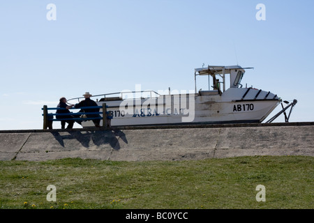 Zwei alte Männer sitzen auf einer Bank am Meer Blick auf einem Boot Stockfoto