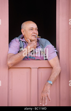 Kubanische Mann einer kubanischen Zigarre an der Tür zu seinem bunt bemalte Kolonialhaus. Trinidad, Kuba. Stockfoto