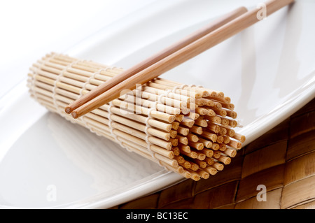 eine geneigte horizontale Makro ein paar Stäbchen und ein Sushi Rollen Matte auf einem weißen Teller Stockfoto