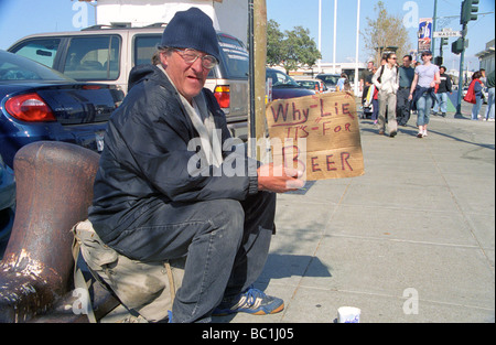 Obdachloser auf einem Bürgersteig sitzt auf einer Tasche mit einem Schild, das Warum liest es s für Bier liegen Stockfoto