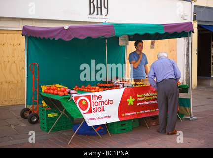 Tomatenverkäufer von der Insel Wight auf dem englischen Farmers Market in der North Street, Chichester, West Sussex, Großbritannien mit Backsteine und Mörsergeschäft hinter der Grenze Stockfoto