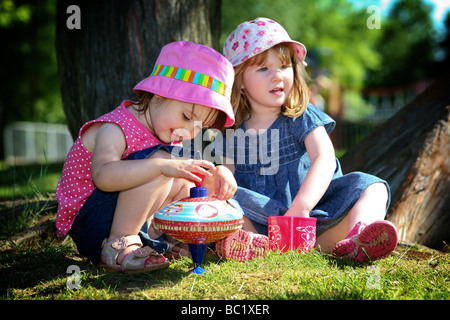 Zwei Pre-school Kleinkinder Kleinkinder Mädchen beste Freundinnen spielen mit Spinnign oben und Stapeln Tassen unter schattigen Baum im park Stockfoto