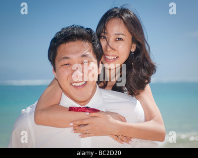 Asiatische Braut reitet auf dem Rücken ihres Mannes in einem spielerischen Moment während ihrer Wanderung entlang Lanikai Beach, Kailua, Hawaii Stockfoto