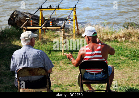 Zwei alte Männer sitzen und reden beim Ansehen 3 Angelruten für Bisse an einem See in Oklahoma, USA. Stockfoto