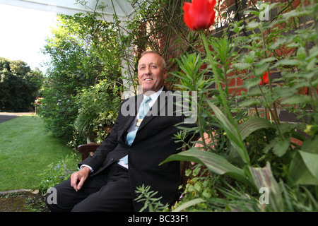 ein Porträt von einem Butler in einem Garten von einem stattlichen Haus lächelnd sitzt und schaut in die Kamera mit einer roten Rose im Vordergrund Stockfoto