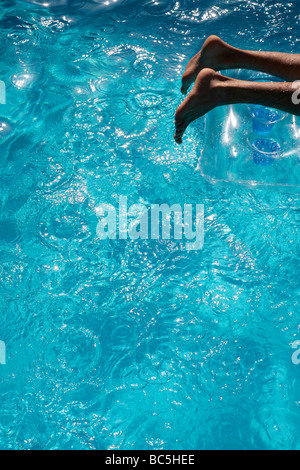 Mans Füße auf einem Lilo in einem blauen Swimmingpool Stockfoto