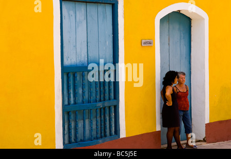 Zwei lokale Frauen reden in Tür gegen helle gelbe Wand des Gebäudes der alten Kolonialstadt Trinidad in Kuba Stockfoto