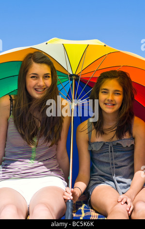 Vertikale Porträt von zwei jungen Schwestern, die sich von der Sonne unter einem riesigen bunten Schirm an einem Sommertag Abschirmung Stockfoto