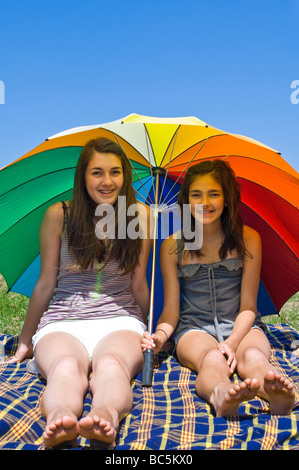 Vertikale Porträt von zwei jungen Schwestern, die sich von der Sonne unter einem riesigen bunten Schirm an einem Sommertag Abschirmung Stockfoto